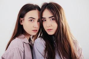 Cute girls looking into the camera. Two sisters twins standing and posing in the studio with white background photo