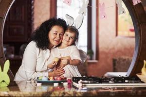 In bunny ears at the head. Grandmother and granddaughter have fun at the kitchen at easter time photo