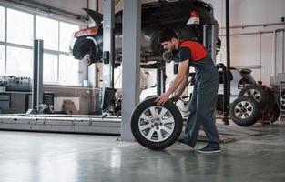Busy guy. Mechanic holding a tire at the repair garage. Replacement of winter and summer tires photo