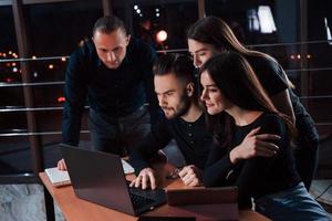 Using the touchpad to search the useful information. Team of young business people works on their project at night time in the office photo