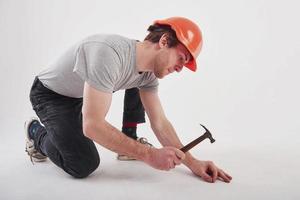 Careful with instrument. Man in casual clothes and orange colored hard hat have some work using hammer. White background photo