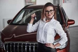 It's yours now. Woman in eyewear and white shirt stands near the red automobile photo