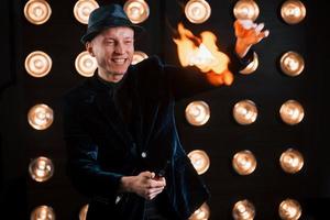 Professional magician showing trick and playing with fire. Light bulbs on background