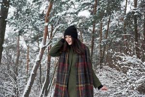 Holidays season. Cheerful young girl in warm clothes have a walk in the winter forest at daytime photo