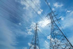 pilón eléctrico de alto voltaje y cable eléctrico contra el cielo azul y las nubes blancas. vista inferior del poste eléctrico con luz solar. torre de red de alto voltaje con cable de alambre. concepto de potencia y energía. foto