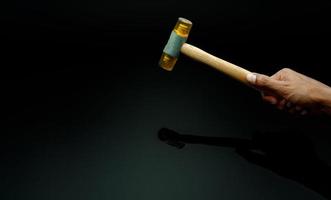 Man's hand holding plastic hammer isolated on dark background. Male worker's hand hold wood handle of plastic hammer. Hammer head made of soft and tough yellow plastic that not damage workpiece. photo