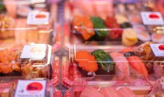 Selective focus on sushi set in plastic box display in shelf at supermarket. Japanese food for take away. Sushi delivery business. Healthy food ready to eat in disposable plastic container. Lunch box.