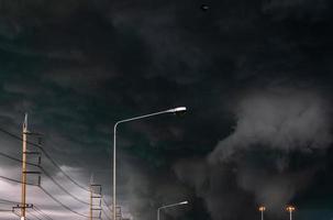 Stormy sky with street light pole and three-phase electric pylons. Stormy sky and dark clouds. Spotlights are open. Storm is coming. Bad weather. Climate change. Overcast sky. Beauty in nature. photo