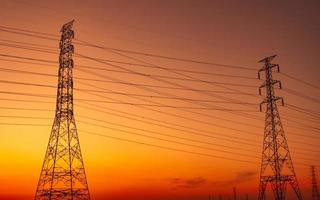 High voltage electric pylon and electrical wire with sunset sky. Electricity poles. Power and energy support factory concept. High voltage grid tower with wire cable. Beautiful red-orange sunset sky. photo
