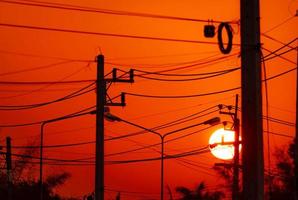poste eléctrico y líneas de transmisión por la noche. torres de alta tensión con cable de alambre y poste de luz de la calle al atardecer. Poder y energía en la ciudad rural. hermoso cielo rojo de puesta de sol detrás de postes eléctricos. foto