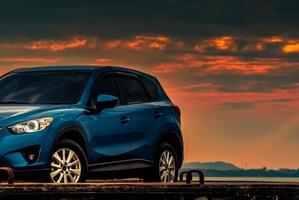 coche suv compacto azul con diseño deportivo y moderno estacionado en una carretera de hormigón junto a la playa al atardecer. tecnología de coches híbridos y eléctricos. plaza de aparcamiento. industria automotriz. antecedentes comerciales de cuidado de automóviles. foto