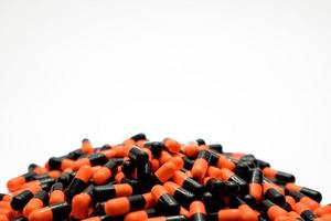 Closeup pile of orange-black capsule pills on white background. Vitamins and supplements. Pharmaceutical industry. Global healthcare concept. Capsule pills production. Drug over use in health system. photo