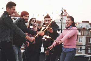 Feeling happy. Playing with sparklers on the rooftop. Group of young beautiful friends photo