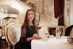 Sincere smile. Attractive young girl sits in beautiful restaurant in vintage style with piano on the stage photo