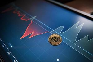 Picture of golden bitcoin lying on the display with graphs in office photo