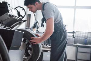 Holds the tire. Young man works with wheel's disks at the workshop at daytime photo