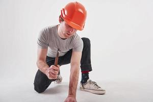 Makes repairs in his own house by himself. Man in casual clothes and orange colored hard hat have some work using hammer. White background photo