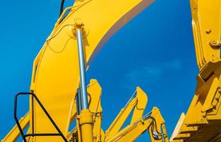 retroexcavadora amarilla con brazo de pistón hidráulico contra el cielo azul claro. máquina pesada para excavación en obra. maquinaria hidráulica. enorme excavadora. industria pesada foto