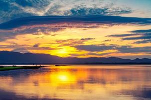 Beautiful golden sky in the morning with sunrise over mountain range and lake or river. Landscape of reservoir and mountain. Peaceful, calm and tranquil background. Stunning and majestic view. photo