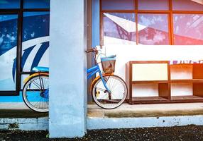 bicicleta apoyada en un poste cerca de un zapatero de madera colocado en un piso de cemento en un edificio con luz de bengala. estilo vintage. foto