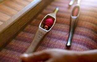 mujer trabajando en una máquina de tejer para tejer tela hecha a mano. tejido textil. tejido en telar manual tradicional sobre hebras de algodón. producción textil o de telas en tailandia. cultura asiática. foto