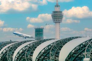 Cargo aircraft flying above airport building. Cargo plane. Air logistic concept. Cargo and shipping business. Freight transportation. The airport building with blue sky and white cumulus clouds. photo