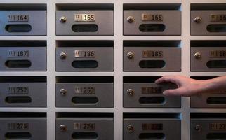 Woman hand open modern mail box of apartment filled home numbers of resident. Mailbox in a row in letter box office of apartment. Post office and envelope mail delivery business concept. Postbox lock. photo