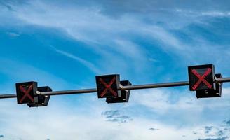 luz de señal de tráfico con color rojo de signo cruzado en el cielo azul y fondo de nubes blancas. signo equivocado ninguna señal de tráfico de entrada. guía de la cruz roja parada ir semáforo. semáforo de advertencia. foto