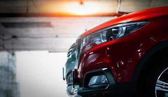 Selective focus on red shiny SUV sport car parked at shopping mall indoor parking lot. Headlamp lights with elegant and luxury design. Automotive industry and hybrid car concept. Underground parking. photo