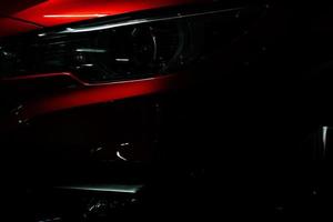 Closeup headlight of shiny red luxury SUV compact car. Elegant electric car technology and business concept. Hybrid auto and automotive concept. Car parked in showroom or motor show. Car dealership. photo