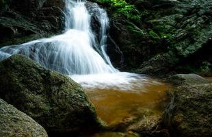 hermosa cascada en la selva. cascada en el bosque tropical con árboles verdes y luz solar. la cascada fluye en la jungla. fondo de la naturaleza. roca o piedra en cascada. fotografía de larga exposición. foto