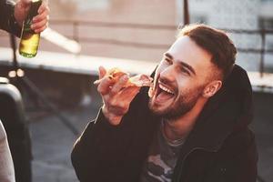 Guy eating a delicious pizza on the rooftop while having party with friends photo