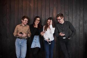 Joking around. Youth stands against black wooden wall. Group of friends spending time together photo