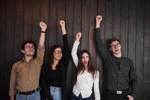 Girl in white shirt screaming. Celebrating succeess. Friends put their hands up against black wooden wall photo