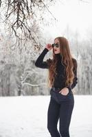 Touching stylish eyewear. Pretty girl with long hair in black blouse and eyewear is in the winter forest photo