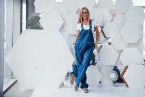 At the break time. Girl in blue uniform stands against abstract wall with white pieces of surface in the shape of hexagon in the auto saloon photo