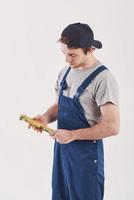 Yellow colored wrench in hands. Man in blue uniform stands against white background in the studio photo