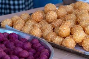 postre tradicional tailandés. bolas de sésamo fritas y bolas de batata fritas en bandeja de acero inoxidable del vendedor. bolas de dulces morados y marrones. foto