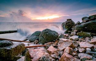 Ocean water splash on rock beach with beautiful sunset sky and clouds. Sea wave splashing on stone at sea shore on summer. Nature landscape. Tropical paradise beach at sunset. Rock beach at coast. photo