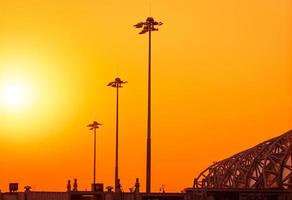 alto pilón eléctrico en el aeropuerto al atardecer con un cielo naranja. poste de focos en el aeródromo. apoyo energético en el concepto del aeropuerto. arquitectura de estructura metálica. postes de luces led para exteriores. foto