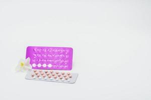 Birth control pills or contraceptive pill with paper case and white flower on white background. Family planning concept. Hormone replacement therapy. Hormonal acne treatment with anti-androgenic pill. photo