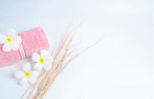 Rolled pink spa towel and Frangipani flowers with branch on white background. Spa and wellness center of the hotel or resort. Background for bath and beauty products. Relax with aromatherapy. Zen. photo