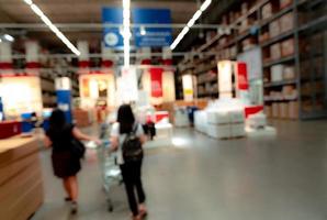 Blurred two woman shopping goods at self-service warehouse of store. Woman pushing a shopping cart in warehouse. Blur rows of shelves with storage box on rack in warehouse. Stock of products. photo