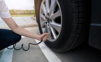 Woman inflates the tire. Woman checking tire pressure and pumping air into the tire of car wheel. Car maintenance service for safety before travel. Tire inflating point. Filling air in the tyre of car photo