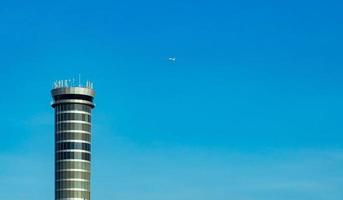 Air traffic control tower in the airport with international flight plane flying on clear blue sky. Airport traffic control tower for control airspace by radar. Aviation technology. Flight management. photo