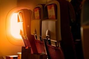 Back view of economy seat with paper brochure insert in box over plastic airplane tray table  . Sunlight passing through the economy class airplane window into the plane. Travel by plane concept. photo