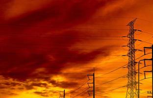 Siluetee la torre eléctrica de alto voltaje y el cable eléctrico con un cielo anaranjado. postes de electricidad al atardecer. concepto de potencia y energía. torre de red de alto voltaje con cable de alambre en la estación de distribución. foto