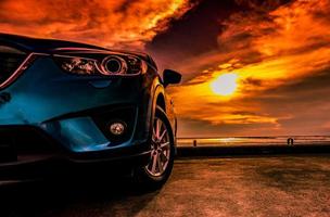 Blue compact SUV car with sport, modern, and luxury design parked on concrete road by the sea at sunset. Front view of beautiful hybrid car. Driving with confidence. Travel on vacation at the beach.