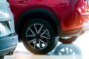 Closeup wheel of red car parked in showroom. Wheel and tire of new car. Car dealership business concept. Auto leasing and car insurance. Automotive industry. New red shiny auto for sale in showroom. photo