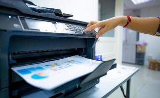 Office worker prints paper on multifunction laser printer. Copy, print, scan, and fax machine in office. Document and paper work. Print technology. Hand press on photocopy machine. Scanner equipment. photo